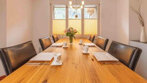 Une salle de conférence avec une table en bois, des chaises noires, des assiettes blanches, des tasses et un vase rempli de fleurs.