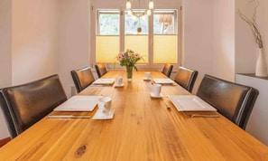 Ein Konferenzraum mit einem Holztisch, schwarzen Stühlen, weißen Tellern, Tassen und einer Vase mit Blumen.