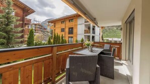 Un balcon agrémenté de meubles en osier, une table avec un vase, et une vue sur les bâtiments et les arbres.