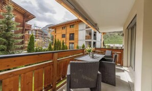 Ein Balkon mit Korbmöbeln, einem Tisch mit einer Vase und Blick auf Gebäude und Bäume.