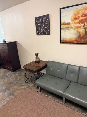 A living room with a grey sofa, a small table with a vase, a dark wooden cabinet, and a framed painting on the wall.