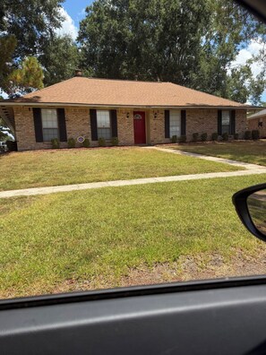A two-story brick house with a red front door, a small front yard, and a visible side window.