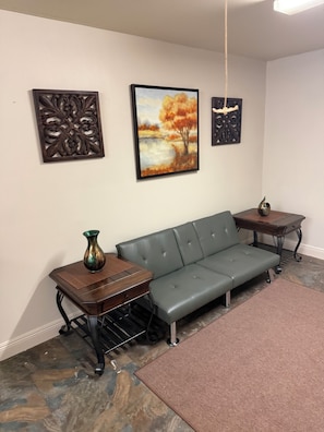 Una habitación con un sofá gris, una pequeña mesa de madera con un florero, y dos elementos decorativos en la pared.