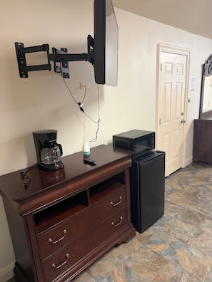 Una habitación con un aparador de madera, una cafetera, un control remoto, un refrigerador negro y un televisor montado.