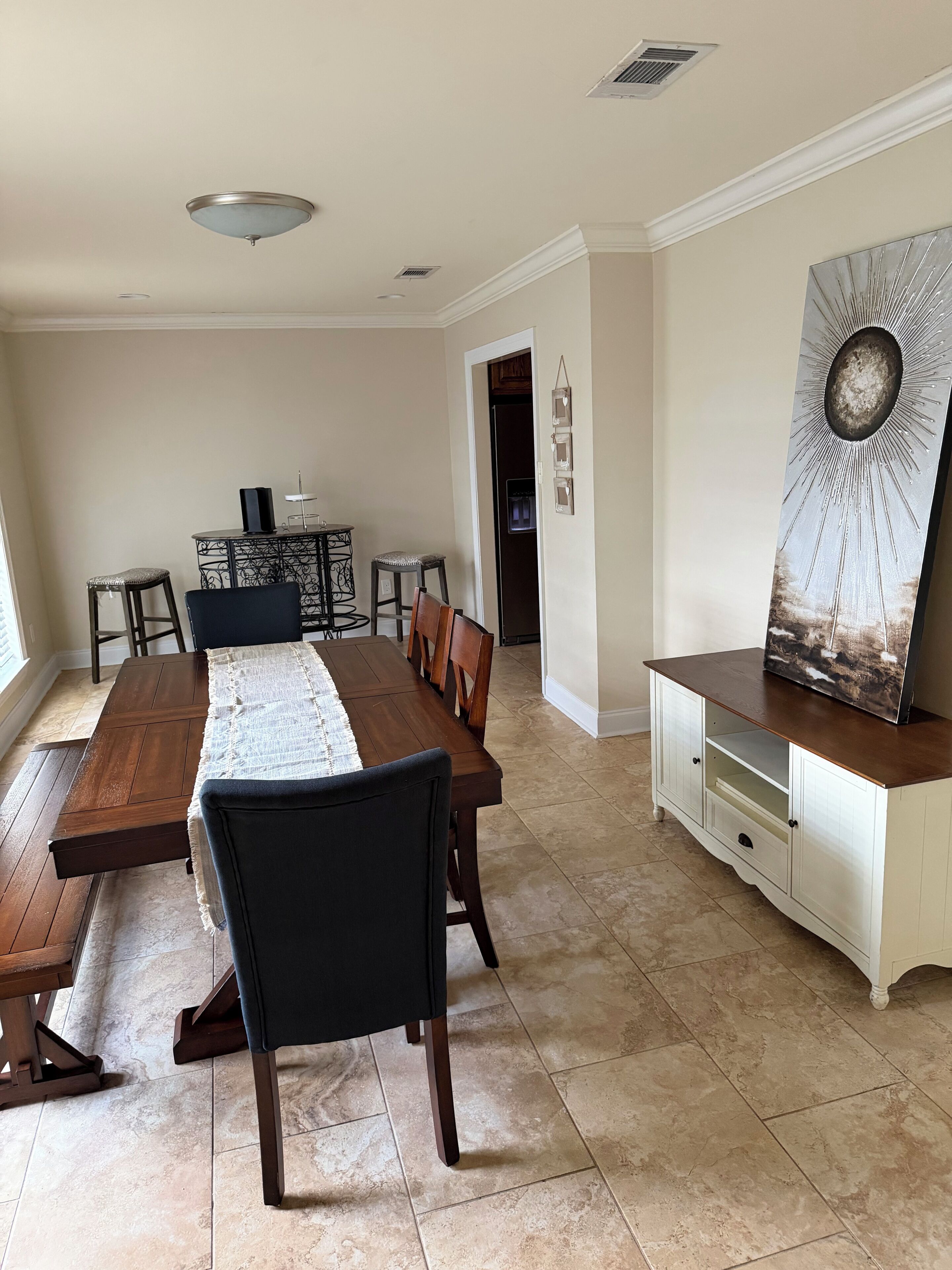 A dining area with a wooden table and chairs, a white cabinet with a decorative piece, and a tiled floor.