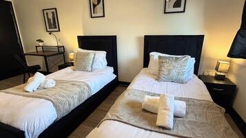Two twin beds with white linens, a bedside table with a lamp, and a framed picture on the wall.
