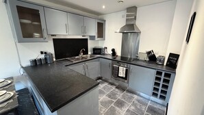 A modern kitchen with grey cabinets, a black countertop, and a stainless steel range hood. - 2BR | 2BA | Manchester |Wi-Fi | Free Gated Parking |Near MRI, MMU, UOM| (Manchester)