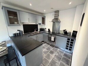 A modern kitchen with grey cabinets, a black countertop, and a stainless steel range hood. - 2BR | 2BA | Manchester |Wi-Fi | Free Gated Parking |Near MRI, MMU, UOM| (Manchester)