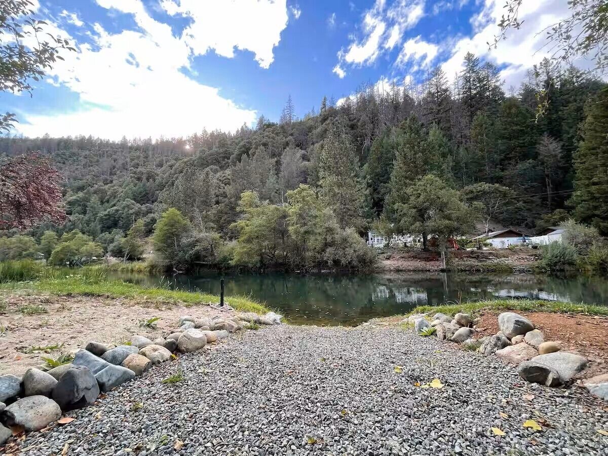 A natural landscape with a lake, surrounded by trees and a rocky foreground.