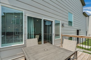 A residential deck with a table and chairs, large sliding glass doors, and a view of the backyard.