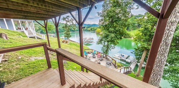 Um deck de madeira com guarda-corpo, vista para um lago, um cais e área de estar ao ar livre.