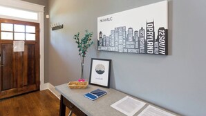 A reception area with a framed city skyline artwork, a potted plant, a wicker basket, and a desk with papers and a notebook. - #3B, Rooftop Deck, Pool Table, 3 mi to Broadway (Nashville)