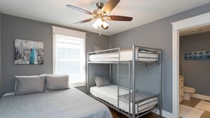 A bedroom with a bunk bed, a single bed, a ceiling fan, a window with blinds, and a bathroom visible through an open door. - #3B, Rooftop Deck, Pool Table, 3 mi to Broadway (Nashville)