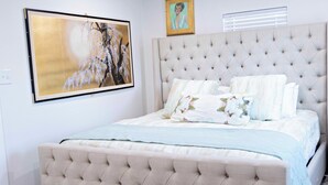 Quarto com cabeceira estofada, cama com várias almofadas e um quadro grande emoldurado na parede.
