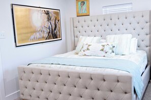 Ein Schlafzimmer mit einem gesteppten Kopfteil, einem Bett mit vielen Kissen und einem großen gerahmten Gemälde an der Wand.