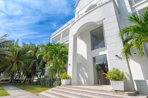 Um edifício moderno com fachada branca, grandes janelas e um jardim bem cuidado com palmeiras.