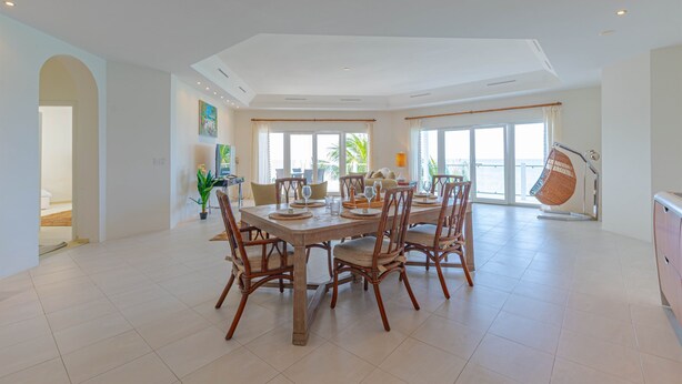 A spacious dining area with a high ceiling, large windows, and a view of the outdoors. - LoveBeach W3 - Luxury Oceanfront Condo + Pool (Nassau)