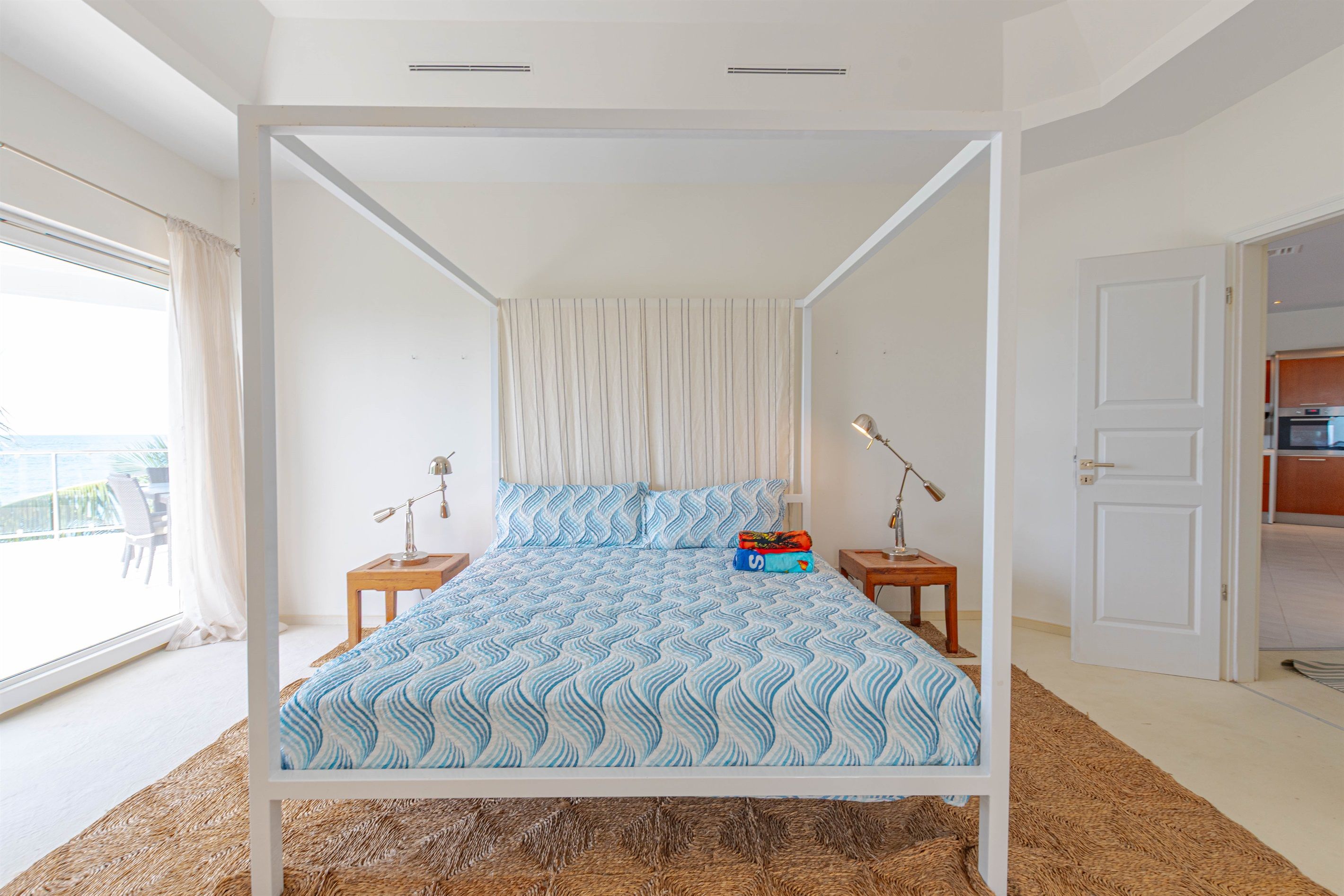 Una cama con dosel, con un edredón estampado, lámparas de noche y vistas al exterior a través de un ventanal grande.