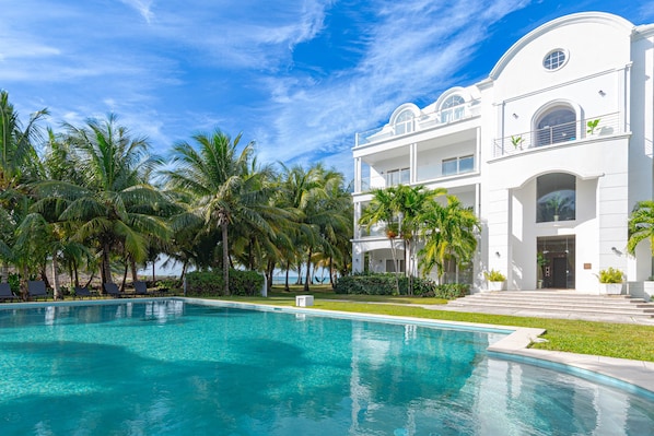 Un hotel moderno con piscina, palmeras y un cielo azul despejado.