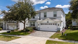 A two-story residential house with a garage, surrounded by well-maintained lawns and trees. - 7BD Home w Pool Game Room Near Parks (ON56) (Championsgate)