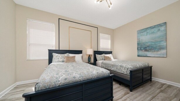 A bedroom with two beds, a ceiling light fixture, and a painting on the wall. - 7BD Home w Pool Game Room Near Parks (ON56) (Championsgate)