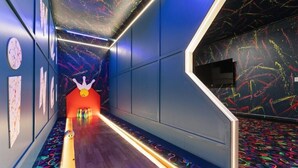 En korridor med en neonupplyst gång, väggar med abstrakta mönster och en röd struktur som liknar en bowlingklot i änden.