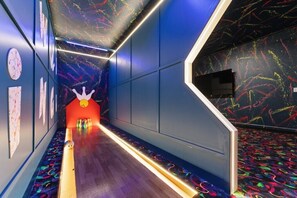Ein Korridor mit einem neonbeleuchteten Weg, Wänden mit abstrakten Mustern und einer roten Struktur, die an eine Bowling-Kegel erinnert, am Ende.