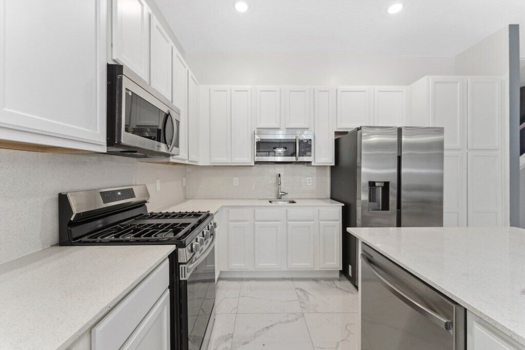 A modern kitchen with white cabinetry, stainless steel appliances, and a marble floor.