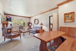 A living room with a fireplace, seating, a dining table, and a painting on the wall. - 2BR 2BA Midway villa with full kitchen, pool view, and resort amenities. (Midway)