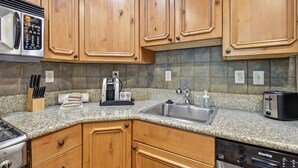 A kitchen with wooden cabinets, granite countertops, a coffee maker, a toaster, and a dishwasher. - 2BR 2BA Midway villa with full kitchen, pool view, and resort amenities. (Midway)
