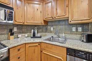 A kitchen with wooden cabinets, granite countertops, a coffee maker, a toaster, and a dishwasher. - 2BR 2BA Midway villa with full kitchen, pool view, and resort amenities. (Midway)