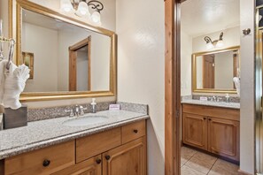 A bathroom with a granite countertop, wooden cabinets, a large mirror, and a towel rack. - Midway Villa with king bedroom, full kitchen, fireplace, pools, and mountain views. (Midway)