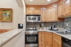 A kitchen with wooden cabinets, a stainless steel stove, a microwave, and a coffee maker. - Midway Villa with king bedroom, full kitchen, fireplace, pools, and mountain views. (Midway)