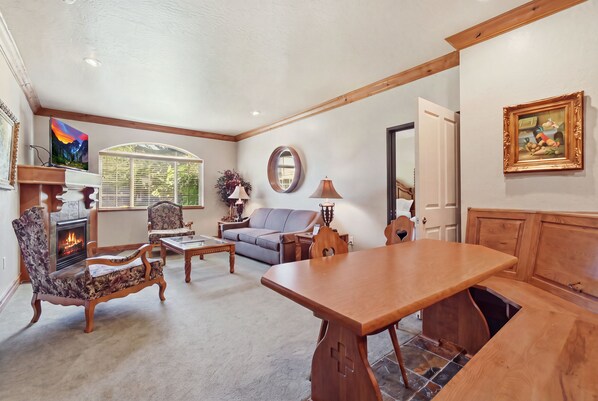 A living room with a fireplace, seating, a dining table, and a painting on the wall. - Midway Villa with king bedroom, full kitchen, fireplace, pools, and mountain views. (Midway)