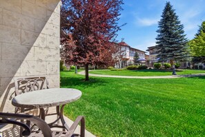 A courtyard with a lawn, a table and chairs, and a building in the background. - Midway Villa with king bedroom, full kitchen, fireplace, pools, and mountain views. (Midway)