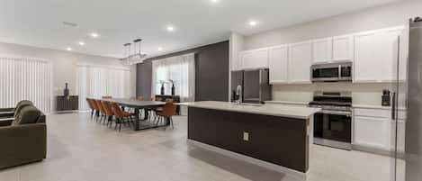A modern kitchen with a central island, built-in appliances, and a dining area with a table and chairs.