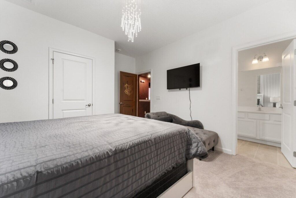 A bedroom with a bed, a television mounted on the wall, and a door leading to a bathroom.