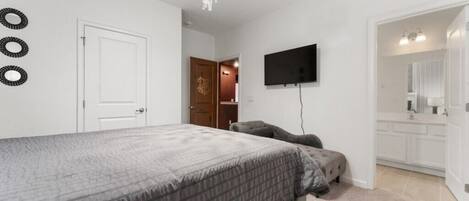 A bedroom with a bed, a television mounted on the wall, and a door leading to a bathroom.