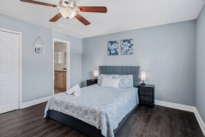 Ein Schlafzimmer mit einem Bett, Nachttischen, einem Deckenventilator und Kunstwerken an der Wand.