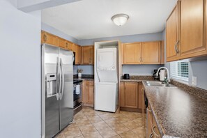 Eine Küche mit einem Edelstahl-Kühlschrank, einem Einbauofen, einer Mikrowelle, Holzschränken, einer Granit-Arbeitsplatte und einem Fenster mit Jalousien.