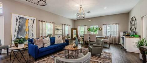 A spacious living room with a blue sofa, a chandelier, and a dining area with a table and chairs.