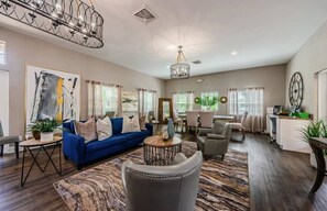 A spacious living room with a blue sofa, a chandelier, and a dining area with a table and chairs. - Fountains of Largo | Perfect Family Vacation Just Minutes from IRB | Communal Pool & Clubhouse (Largo)