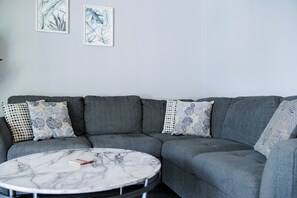 Ein graues Ecksofa mit gemusterten Kissen und einem Marmortisch mit einem Buch.