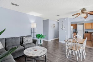 Un salon moderne avec un canapé gris, une table basse en marbre et un coin repas comprenant des chaises blanches et une table en bois.