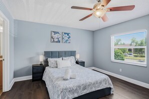 A bedroom with a bed, nightstands, a ceiling fan, artwork, and a window with a view. - Fountains of Largo | Perfect Family Vacation Just Minutes from IRB | Communal Pool & Clubhouse (Largo)