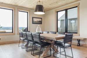 A dining area with a wooden table and black chairs, large windows with views, and a hanging light fixture. - The Lodge at Beach Meadow | Hot Tub + Pickleball (Island Park)