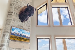 Ein Zimmer mit einer Steinswand, einem aufgehängten Tierkopf und mehreren Fenstern.