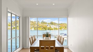 A dining area with a table and chairs, large windows with a view of a lake and houses, and a plant on the table. - The Oatley River House with Jetty & Water Views (Oatley)