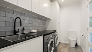 A modern kitchen with a black countertop, stainless steel sink, and a grey brick backsplash. - The Oatley River House with Jetty & Water Views (Oatley)