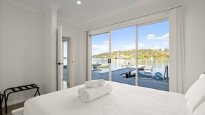 Ein Hotelzimmer mit einem großen Bett, Blick auf Boote auf einem See und einer Tür, die auf einen Balkon führt.